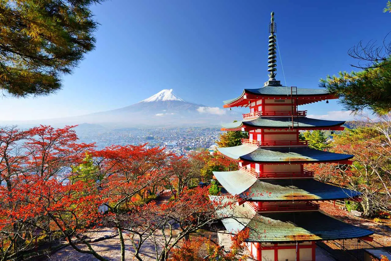 Red and green pagoda surrounded by red foliage, and overlooking snowcapped Mount Fuji in the distance
