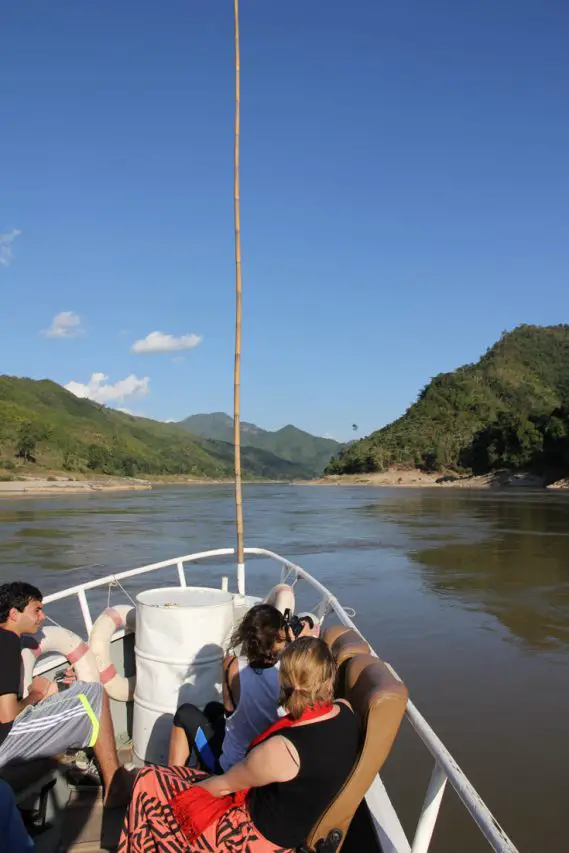 People looking over bow of a boat to a slow moving River and mountainous surrounds