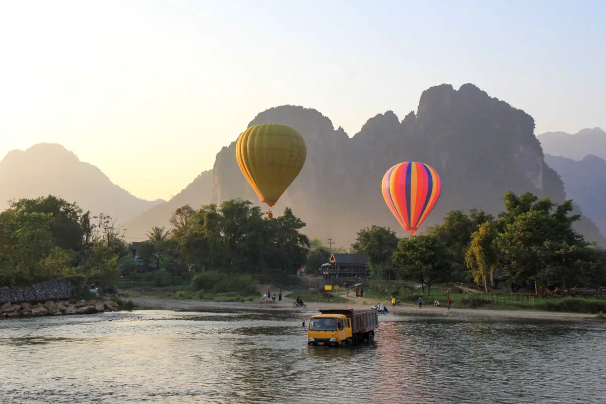 Limestone mountains in background with hot air balloons and river in foreground. Tip truck stuck in the middle of the river.