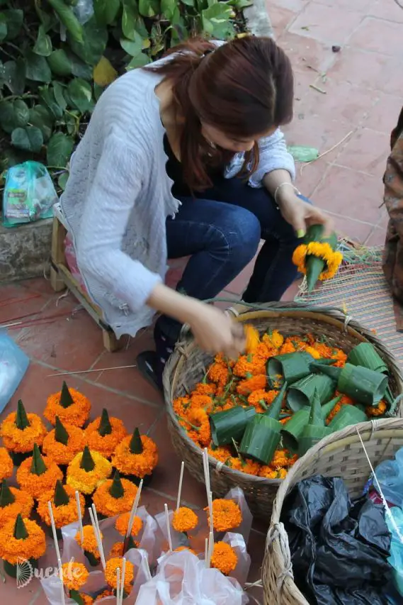 Woman preparing temple offerings from orange flowers and leaves in a basket