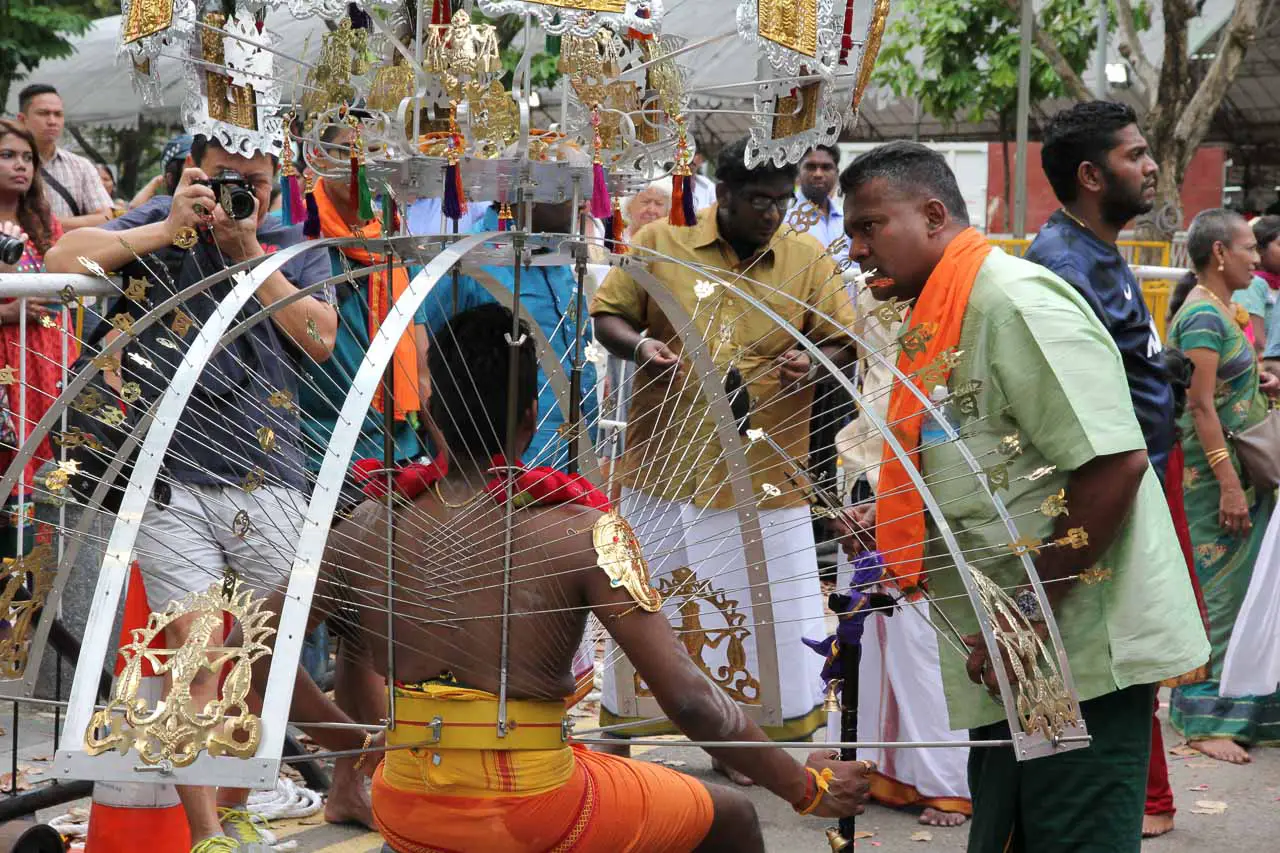 Family rally around man with walking stick kneels to rest on the last steps of his pilgrimage with kavadi
