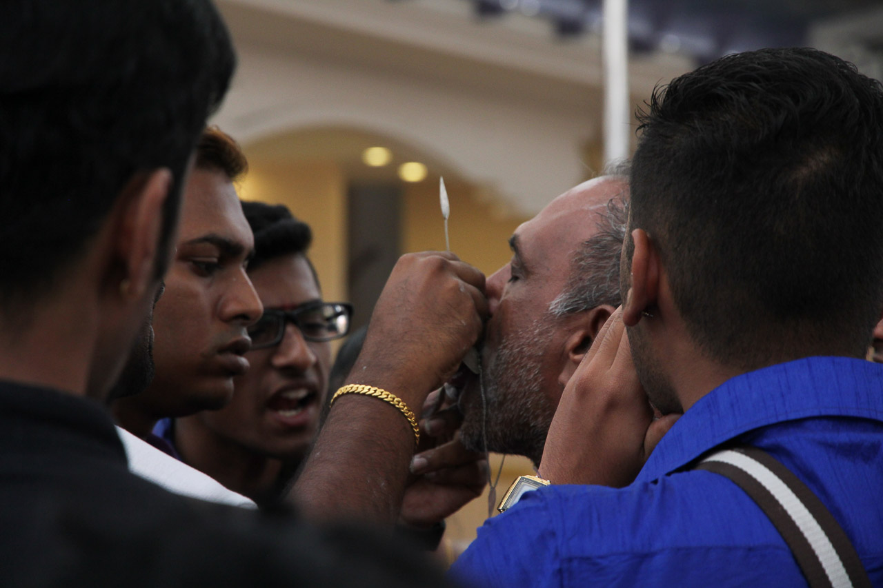 Men huddled tightly, around a man getting his tongue pierced