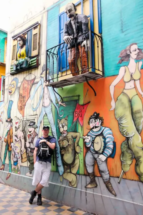 Man with backpack leaning against wall with mural of people