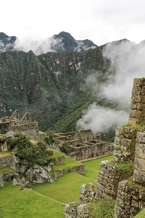 Archaeological site with steep, lush mountains in background and light mist