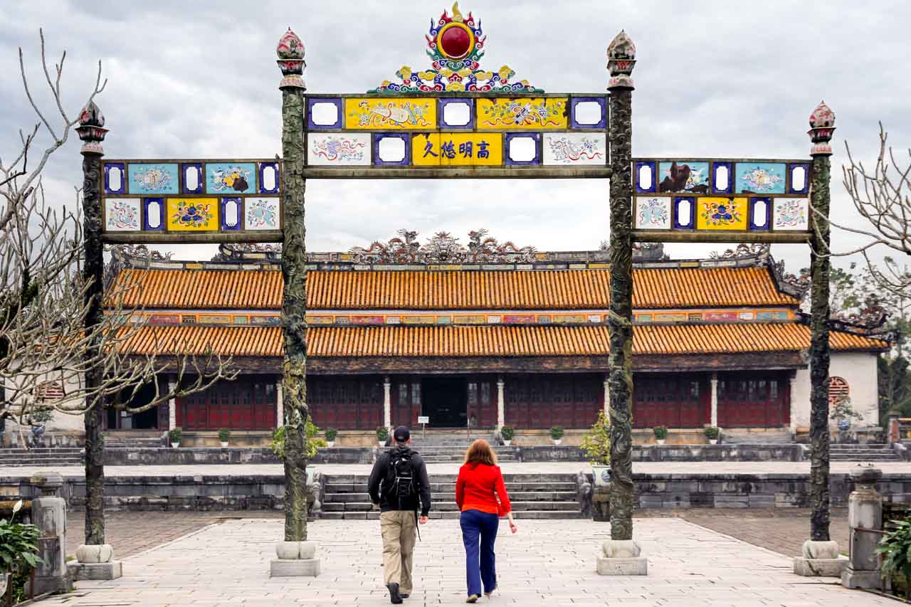 Two people walking through ornamental gate, towards The Palace of Supreme Harmony on a grey, cloudy day