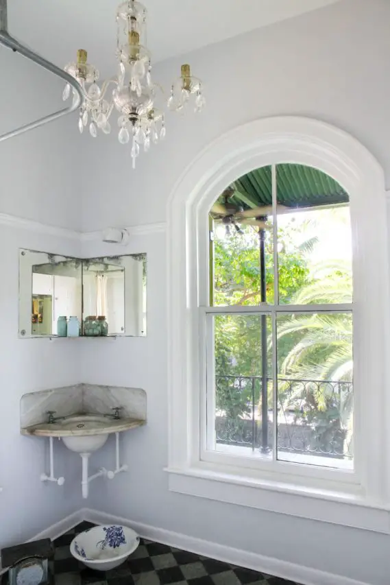 White bathroom with large arched window, corner sink and crystal chandelier