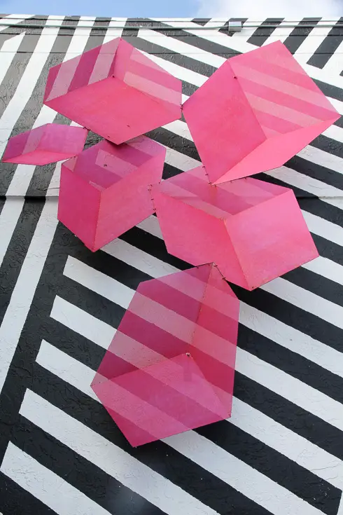 Pink sculpture mounted on black and white striped wall