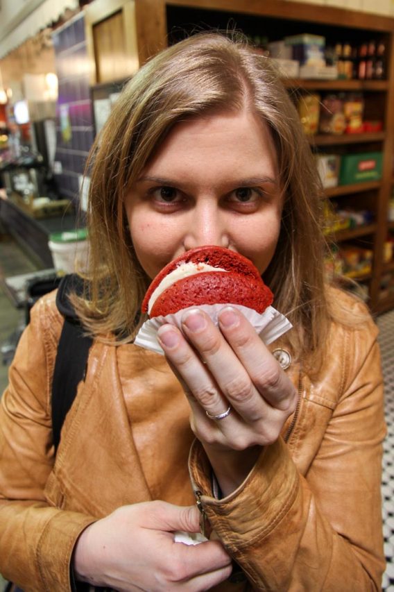 Woman in leather jacket holding red velvet whoopie pie up to camera