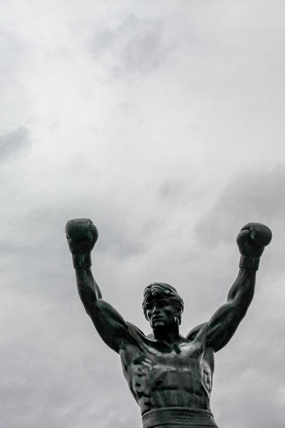 Top half of Rocky Statue with raised arms and boxing gloves against cloudy sky