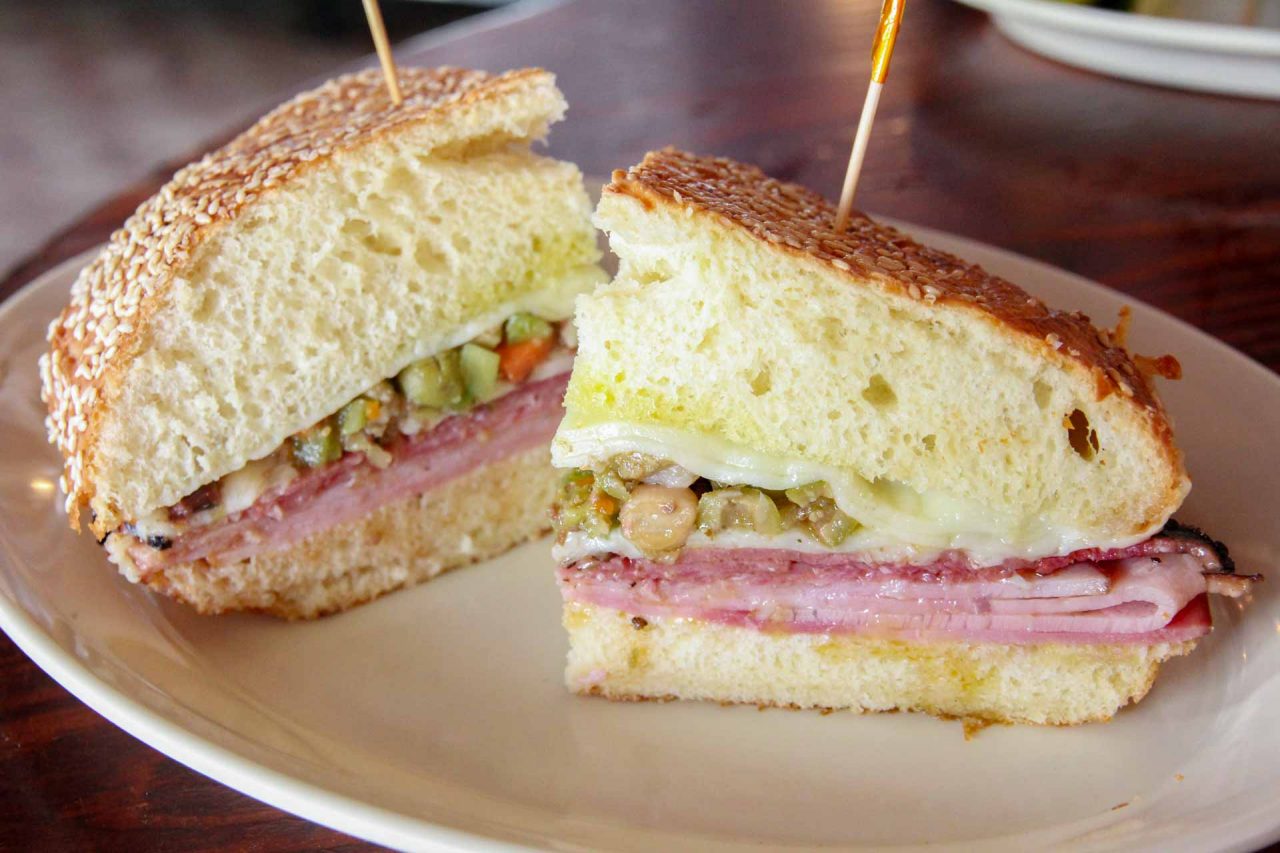 Close up of Muffaletta sandwich served on white plate - Must-Eat New Orleans Foods