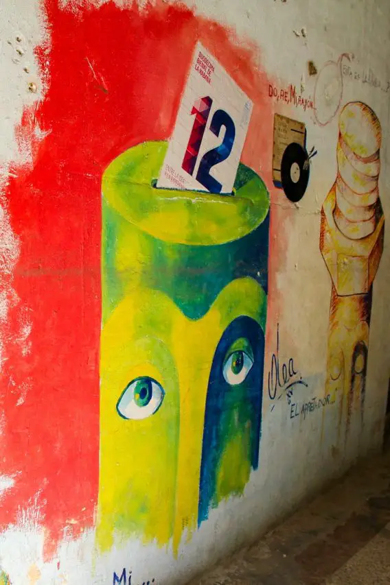 Street art showing green cylindrical face, with dated paper slip being inserted at the top