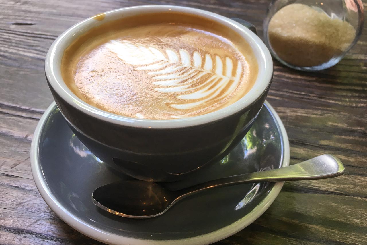 Latte on wooden tabletop with sugar bowl in background