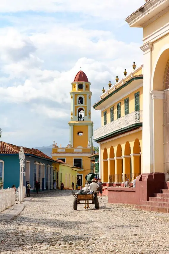 Man in horse and cart travelling down cobblestone street towards a yellow bell tower