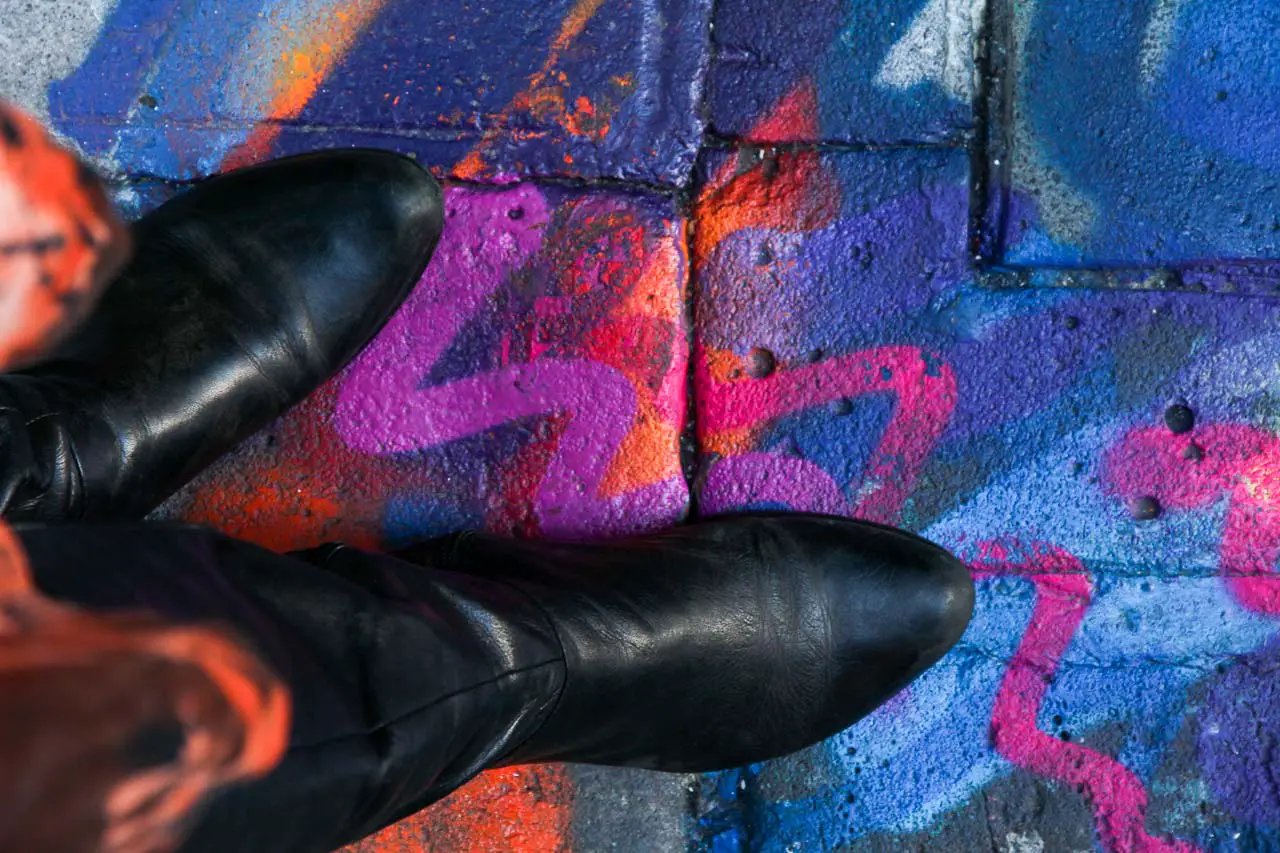 Black boots on a pavement painted in pink and orange squiggles on a blue background.