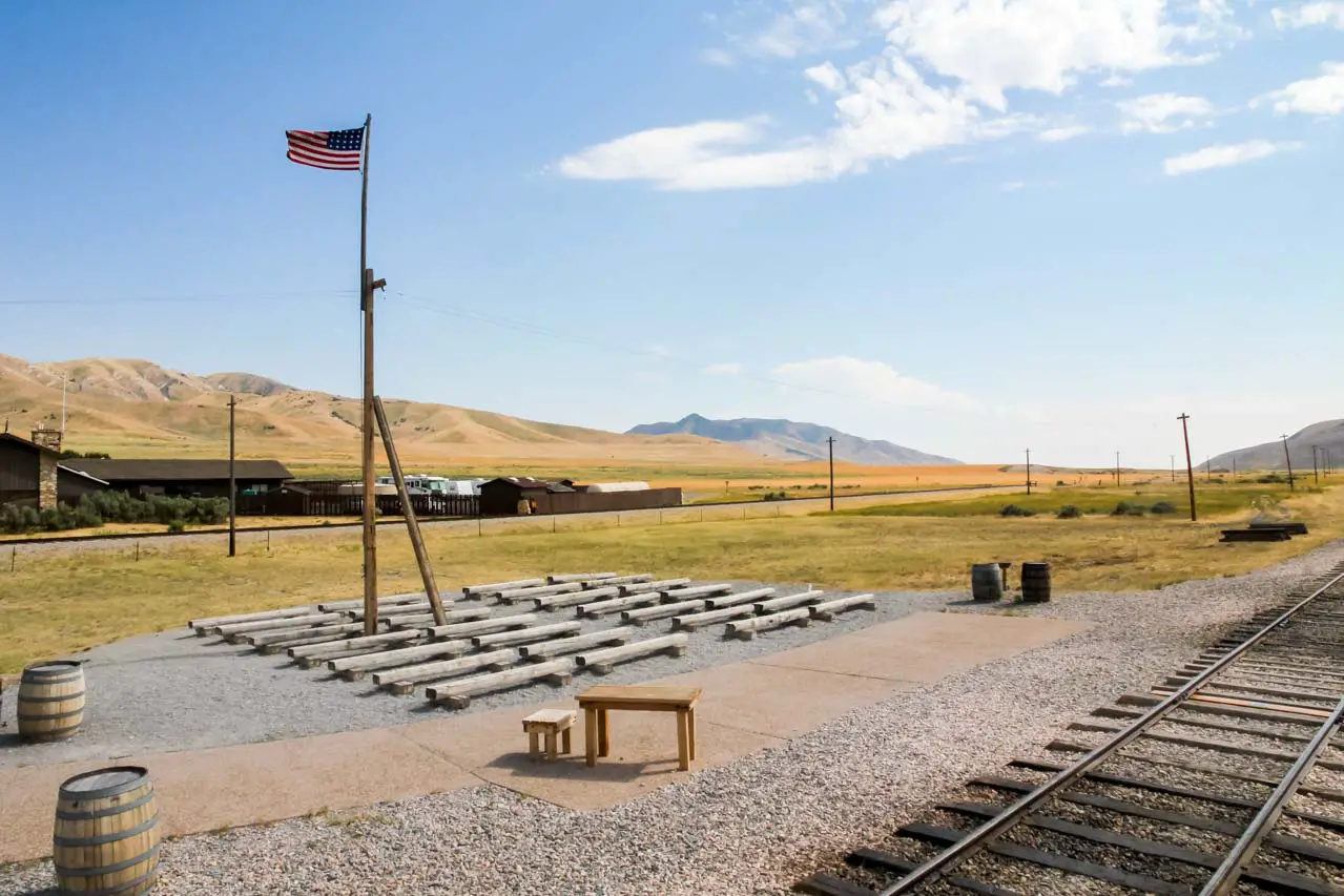 Photo of Golden Spike National Historic Site with railway track, seating and US flag in foreground, and arid landscape in background