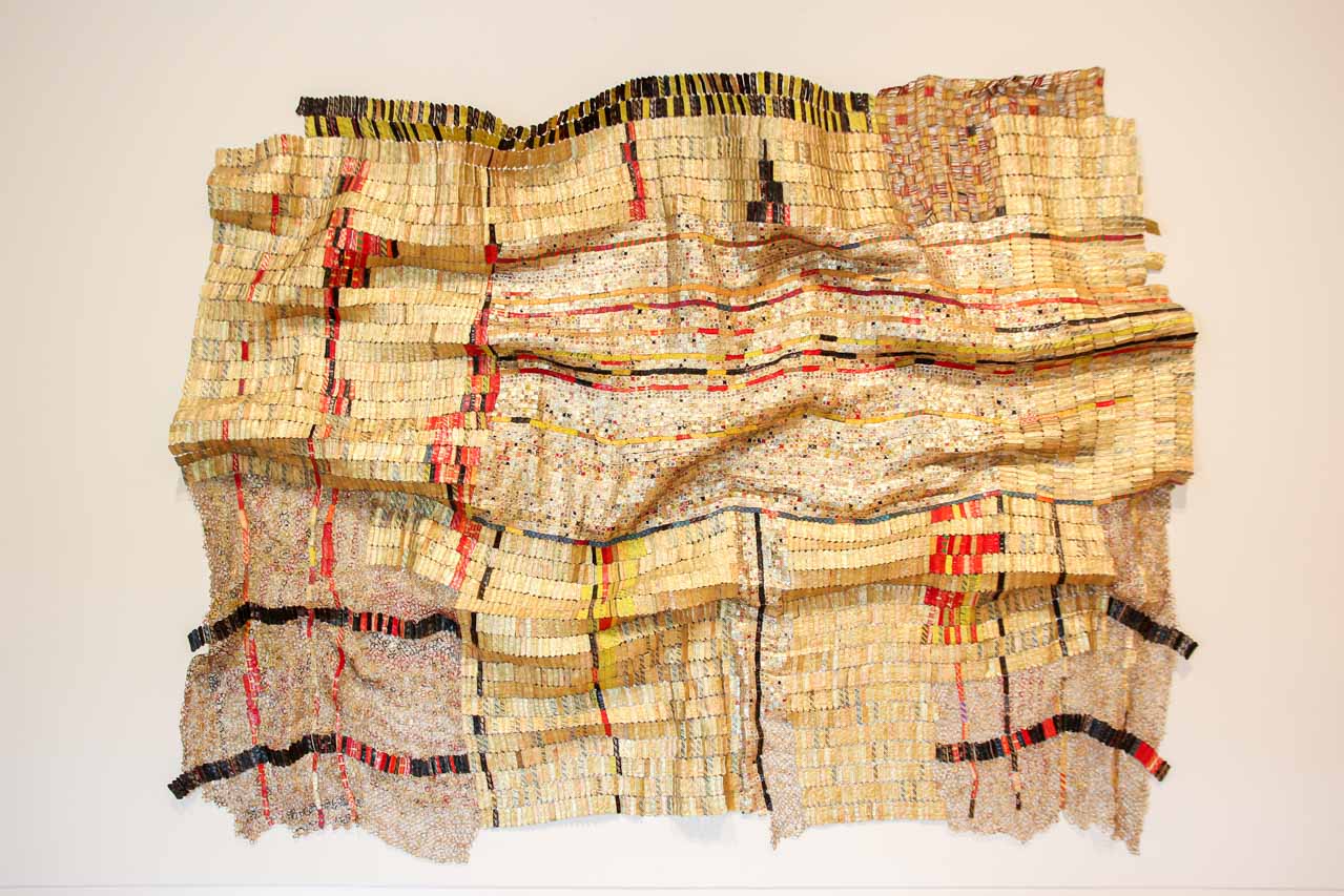 El Anatsui artwork made of metallic bottlecaps hanging on wall.