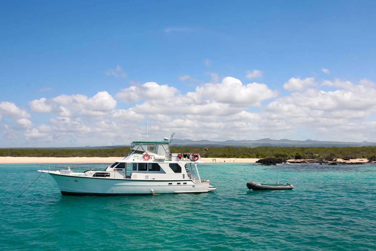 Boat with tender moored off sandy beach with island in background