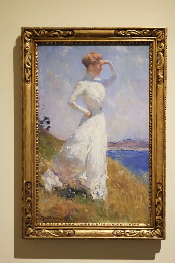Impressionist painting in ornate gold frame of woman looking out over water with her hand shielding her eyes.