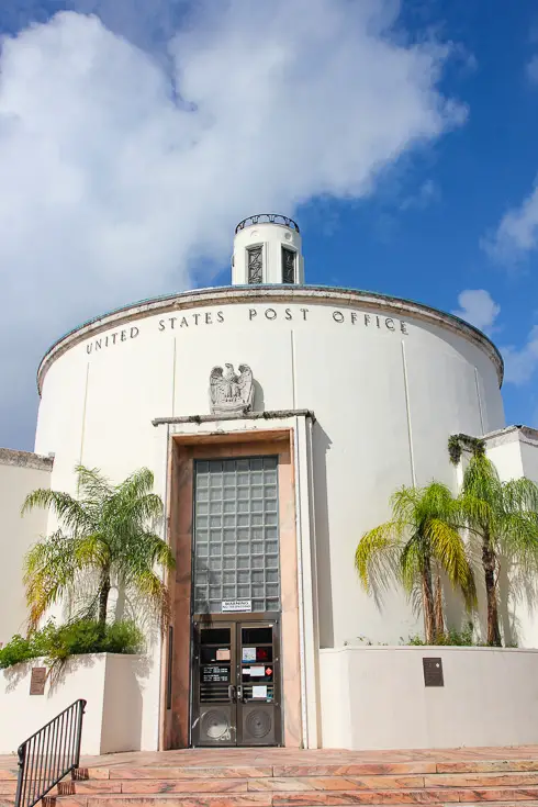 Cylindrical building with glass bricks over engtrance and palm trees at front.