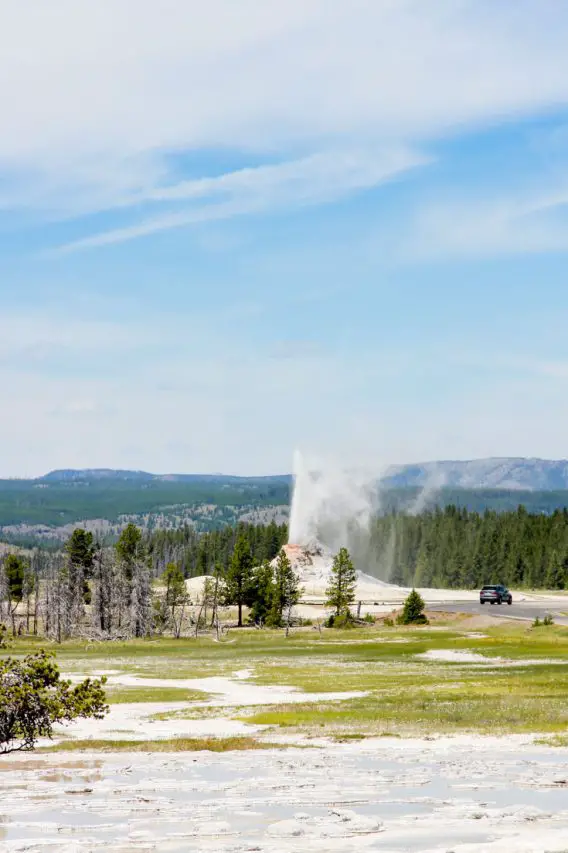 Distant geyser spurting water with a passing car to the right.