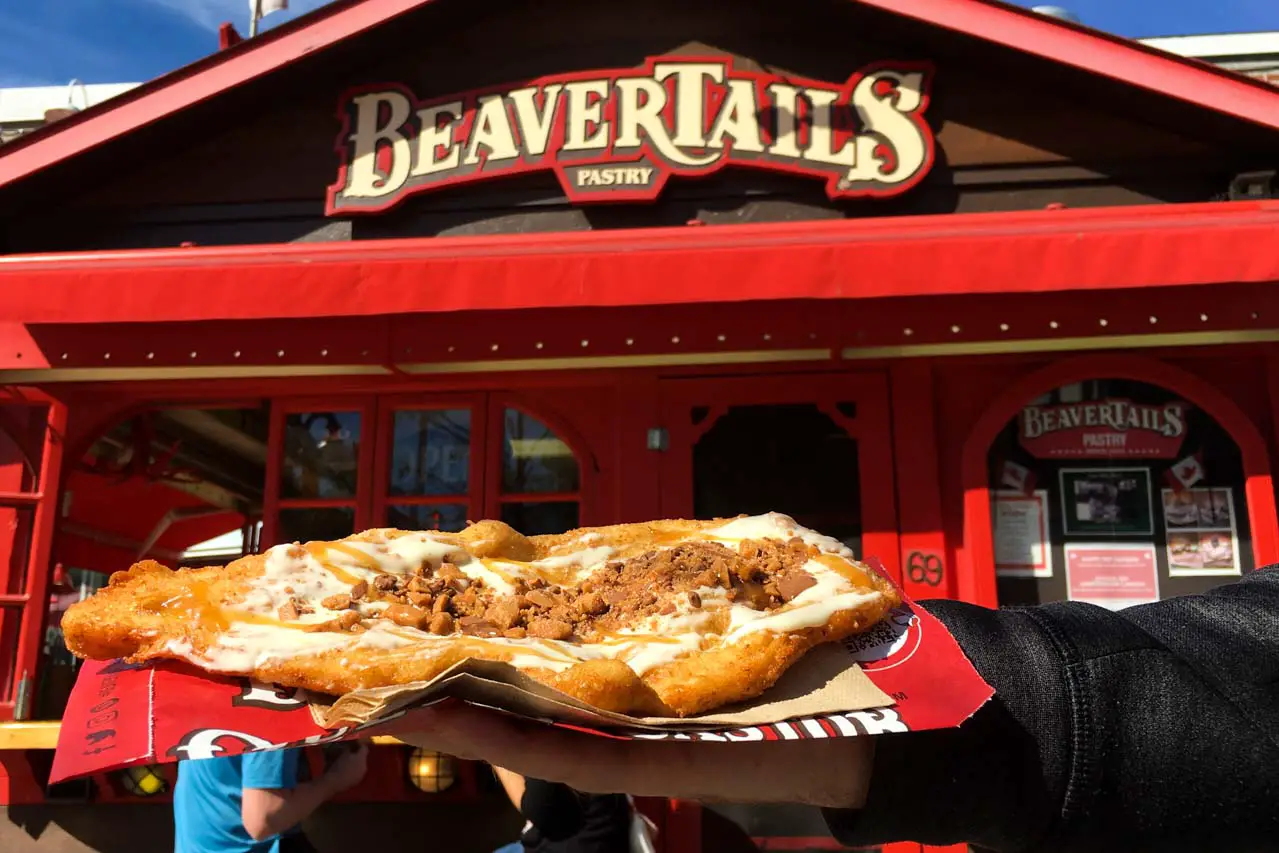 A beaver tail in a person's hand infront of a Beaver Tail store