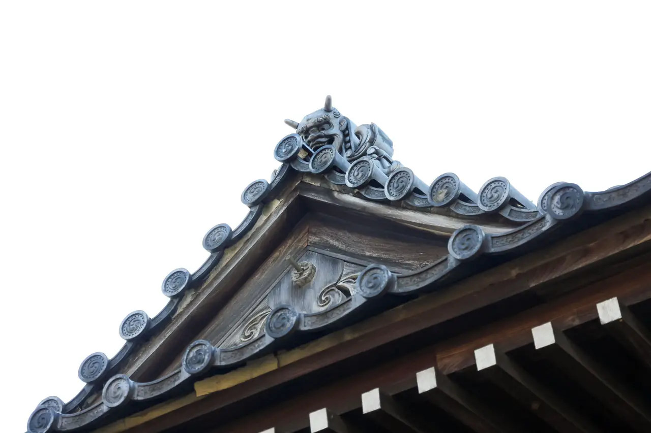 A devilish onigawara peaking over the eaves of a roof in Japan