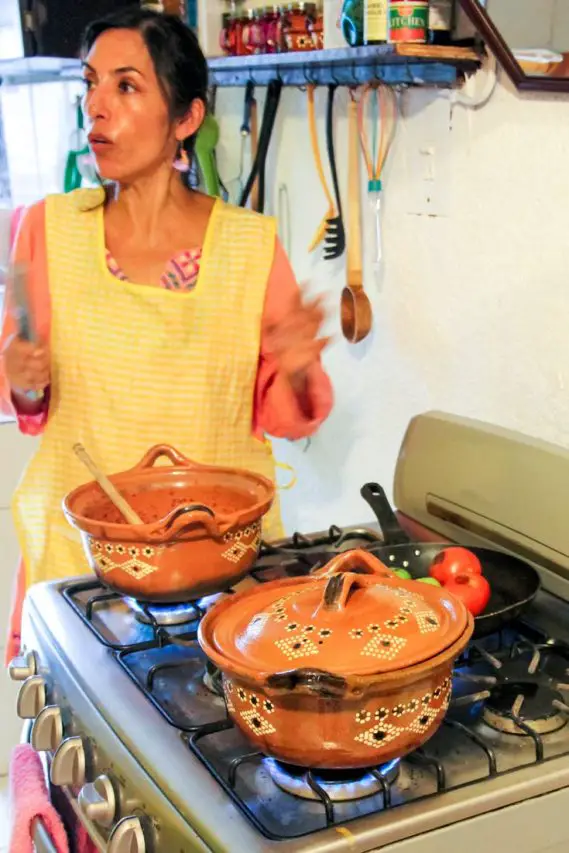 Woman in yellow apron explaining ceramic cookware on stove