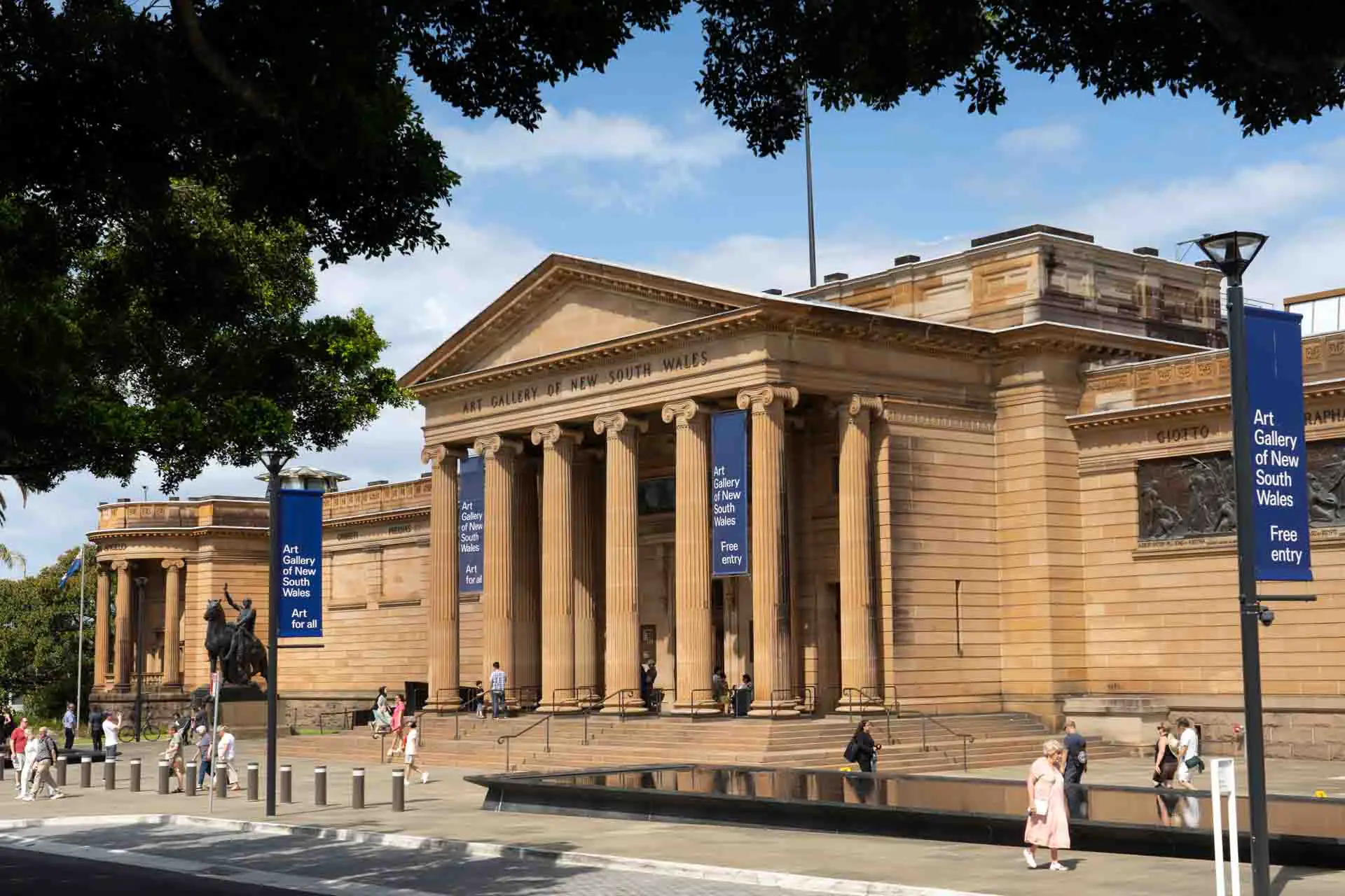 Front facade of Neoclassical building with blue banners reading "Art Gallery of New South Wales"