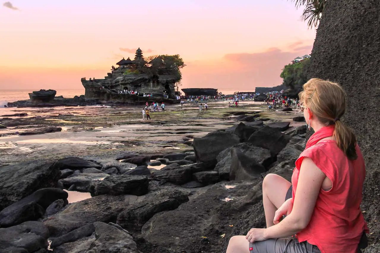 Woman sitting on rock looking at sunset with a silhouette of a Balinese temple