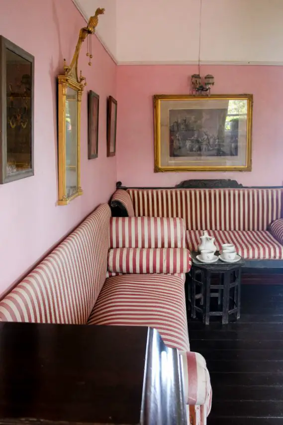 Red striped Victorian chaises, tea set and artworks in a room with pink walls