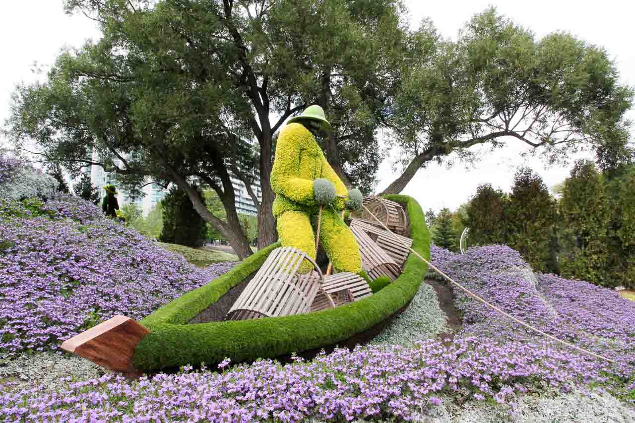 Living sculpture of a lobster fisherman in a boat, on a see of purple flowers