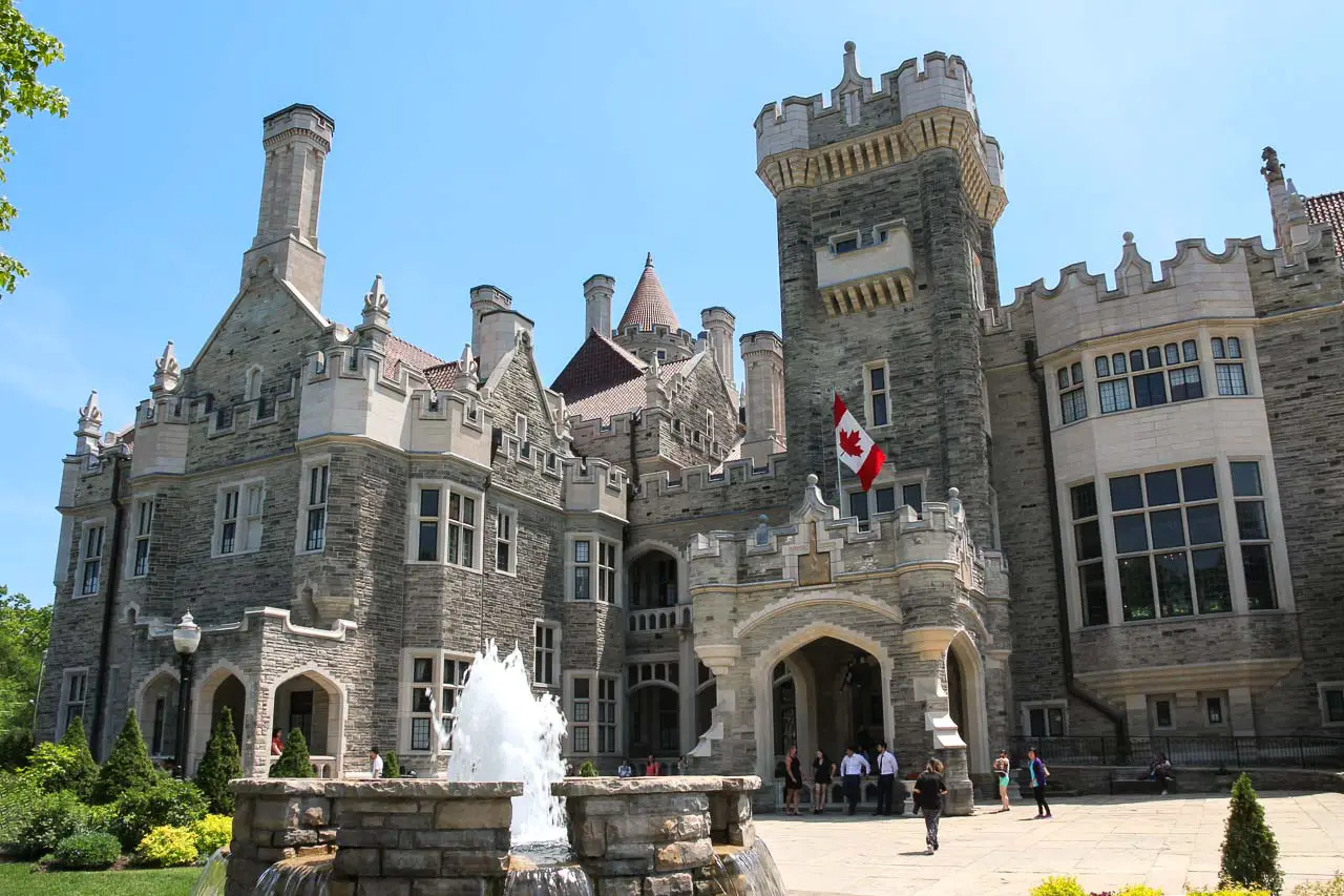 Front entry of large, castle-like mansion with Canadian flag and fountain