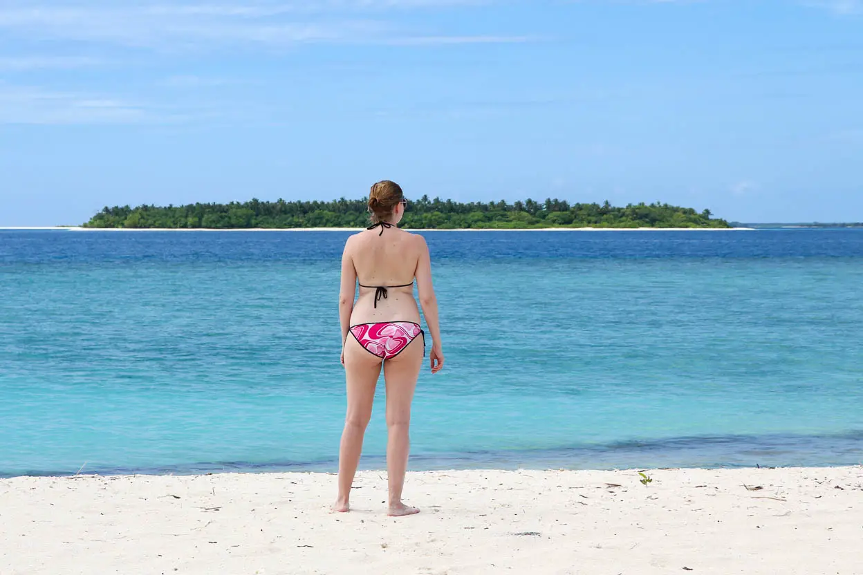 Woman in pink bikini looking out at turquoise water and uninhabitated island in the distance