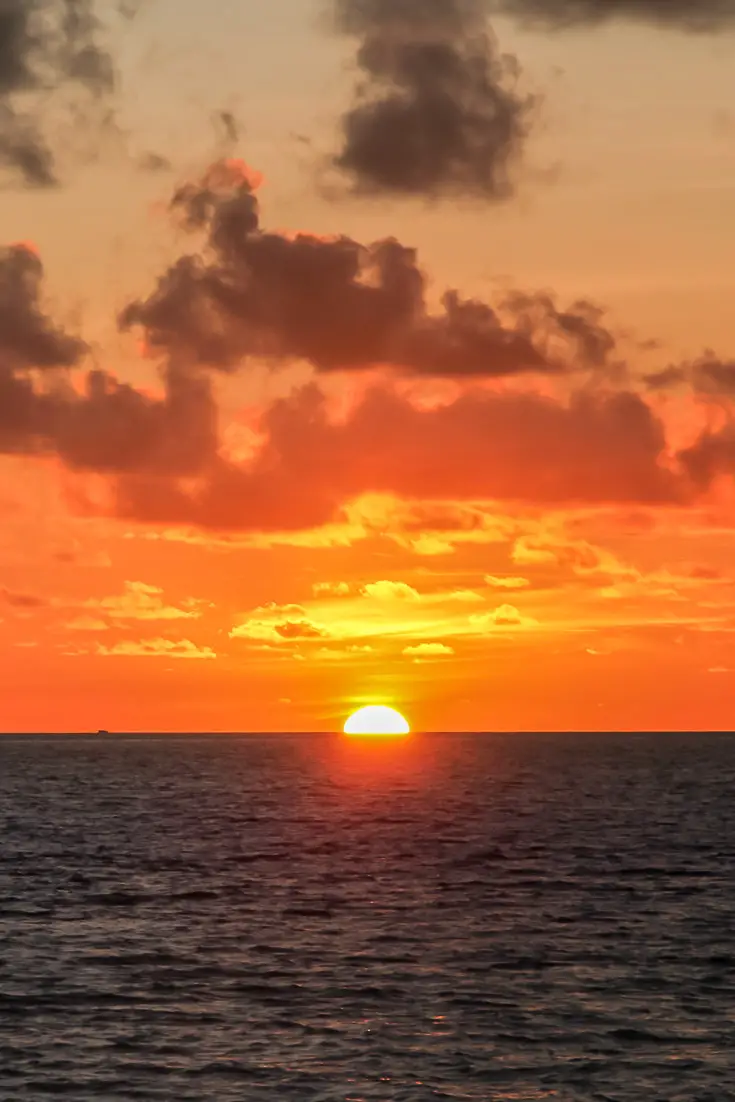 Sunset over ocean with sun partially below horizon and fiery sky.