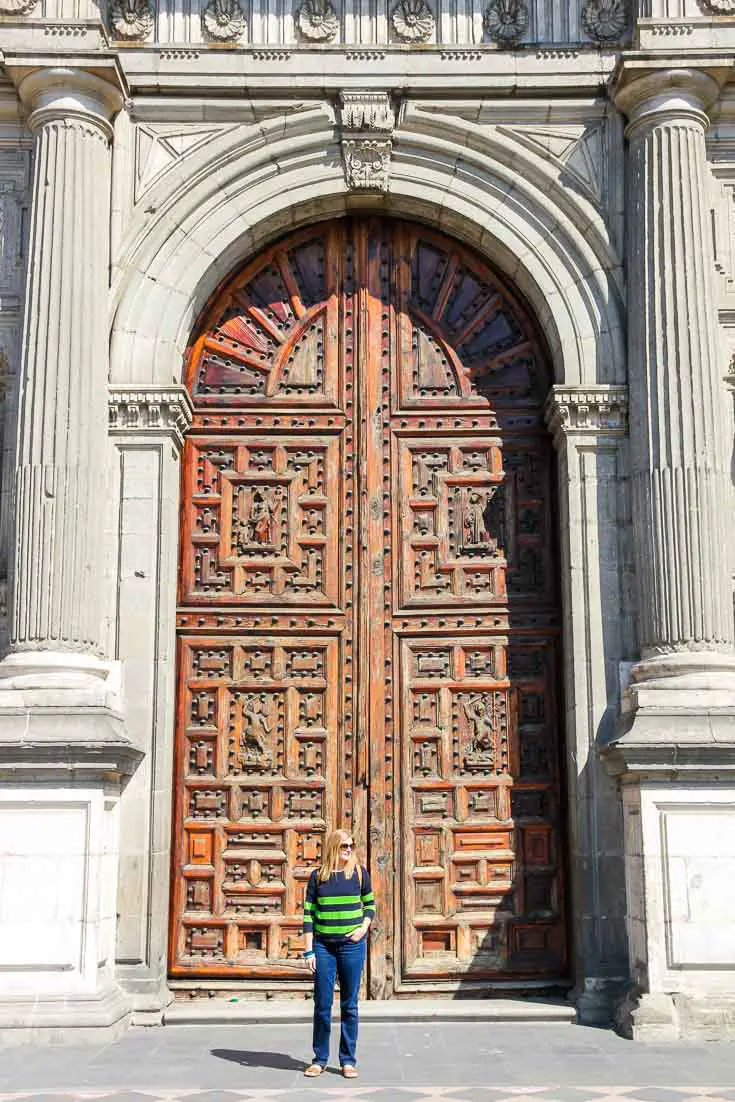 Woman standing infront of ornate building facade with large arched wooden doorway
