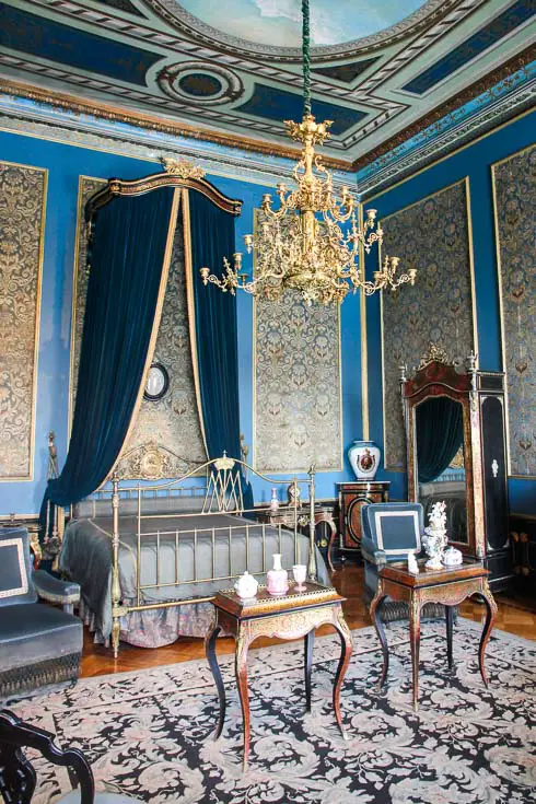 Grand and ornate bedroom with blue and gold details including a large chandelier and canopied bed