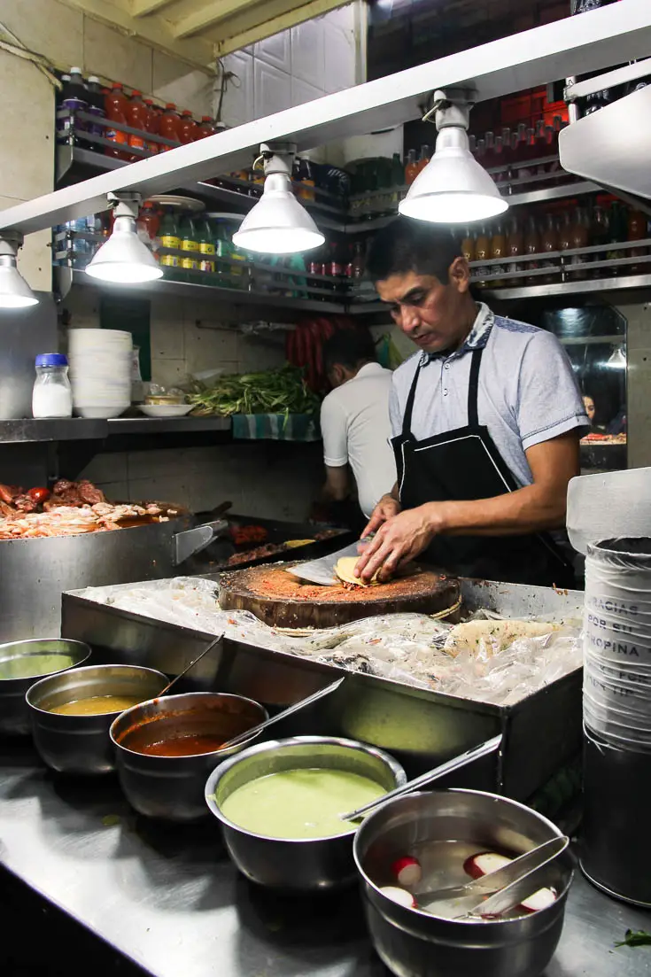 Hole-in-the-wall taqueria with man preparing tacos and a line up of condiments in bowls