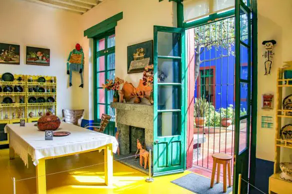 The sunny dining space of La Casa Azul, with bright yellow floor and green French-doors leading out to courtyard