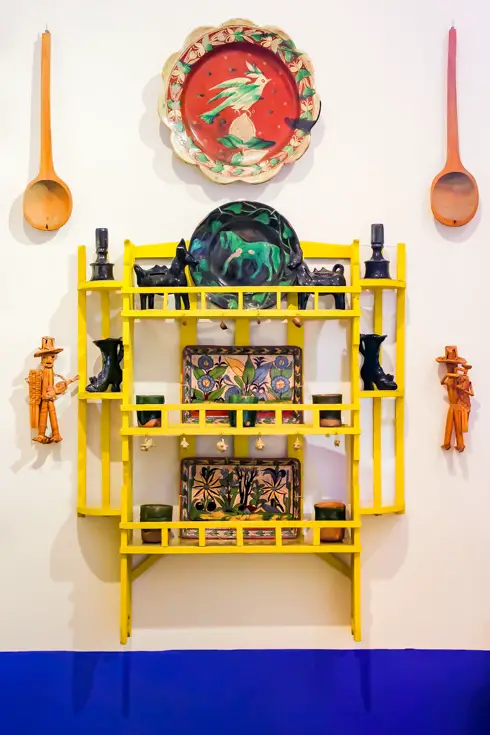 A yellow storage unit hanging on with decorative plates and kitchen utensils