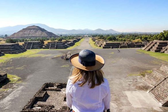 Woman in straw hat looking out over archaeological site including large stone pyramid