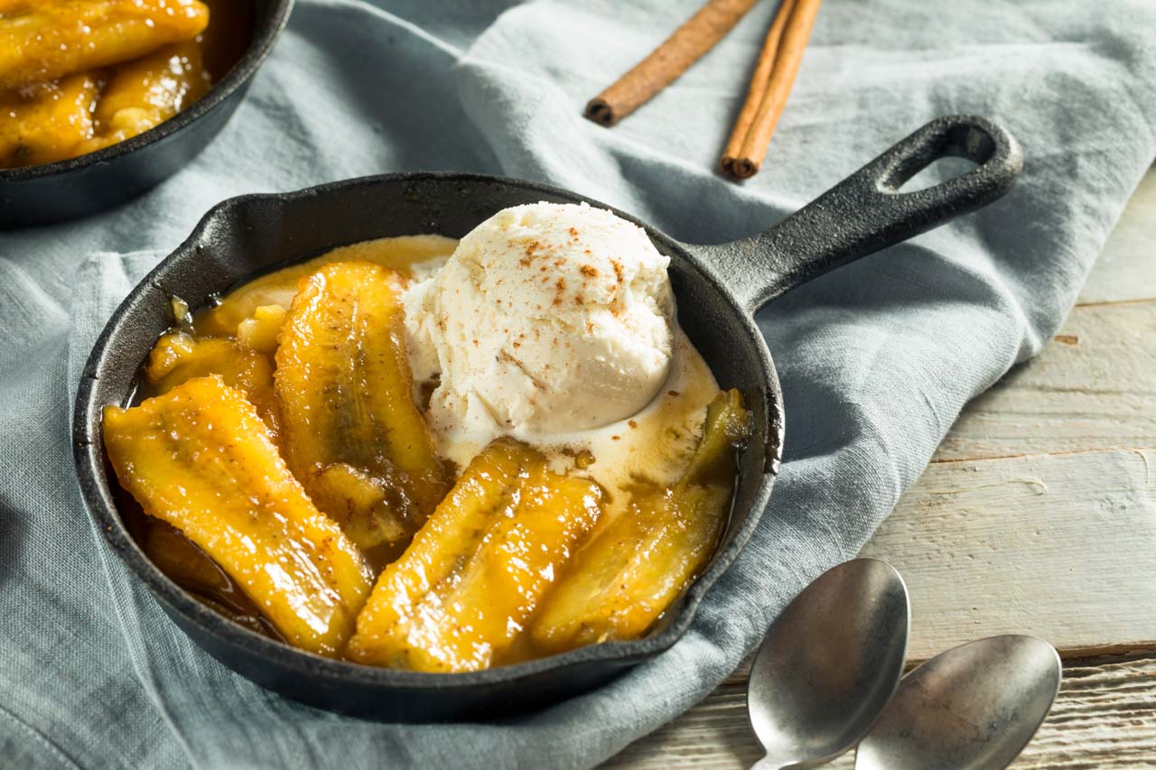 Bananas Foster served in iron skillet on blue linen tablecloth.