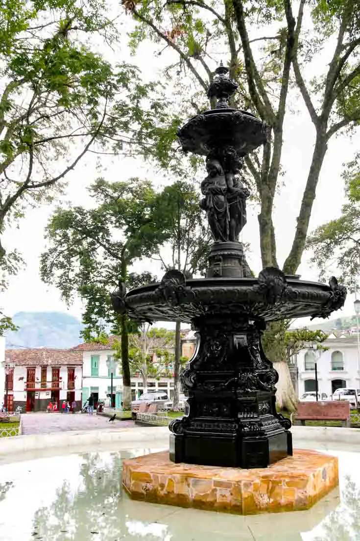 Black fountain in town plaza with colourful buildings and trees