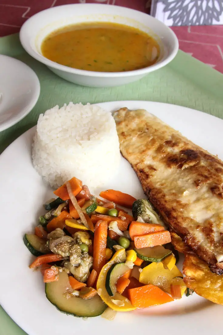 Green tray with bowl of soup, plate of chicken, rice and vegetables