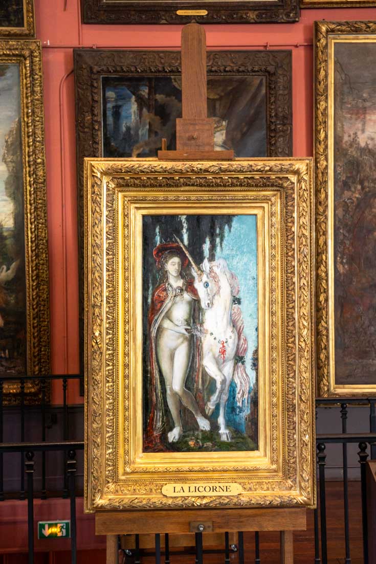 A fairy walks with a unicorn in a painting by Gustave Moreau, framed in gold in his studio turned museum