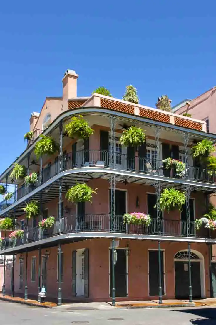 Three-story, terracotta-coloured building with ornate iron verandahs and hanging ferns.
