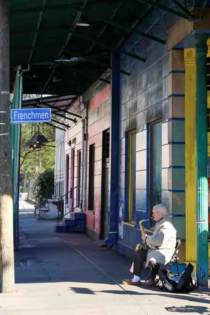 Man playing a saxophone infront of colourful buildings on the corner of Frenchmen Street