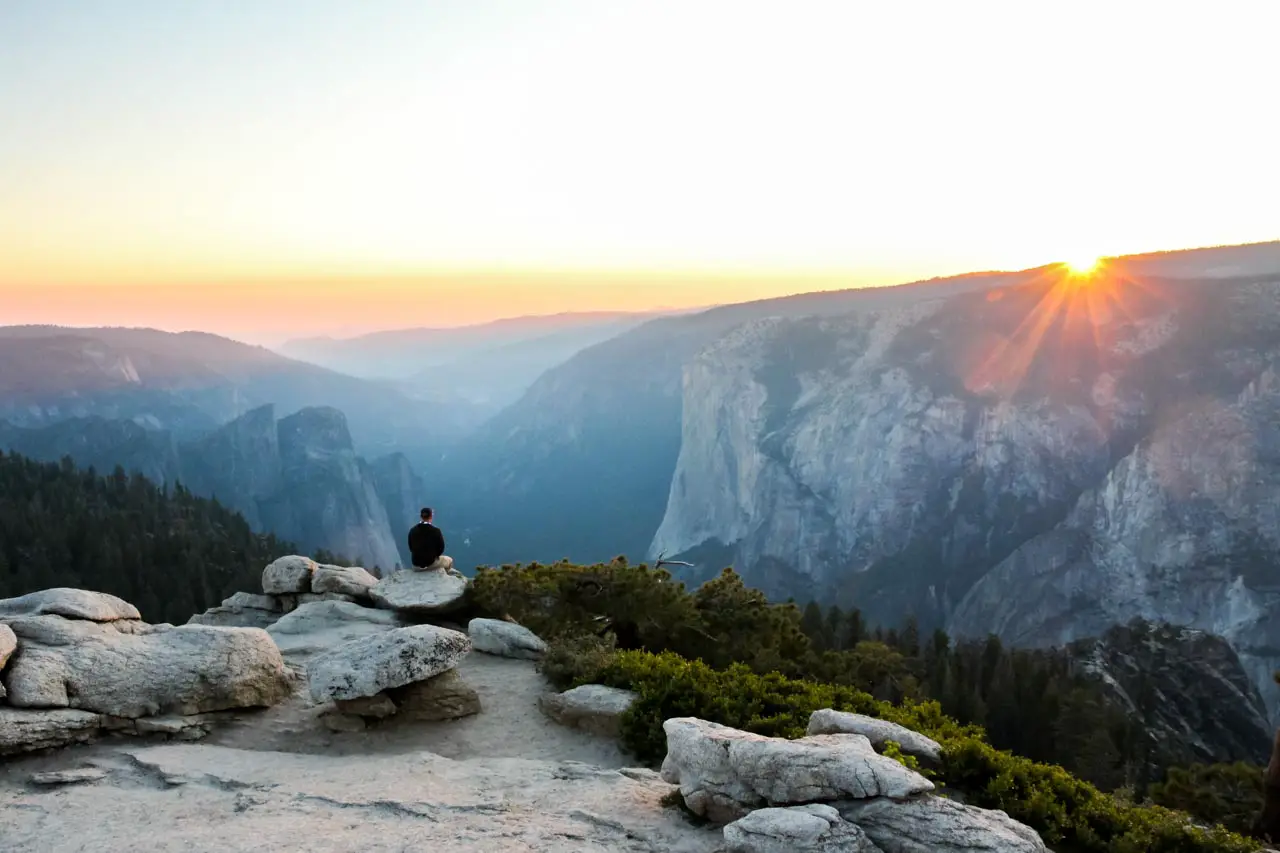 Man sitting on rock looking out over valley with sun dipping below horizon