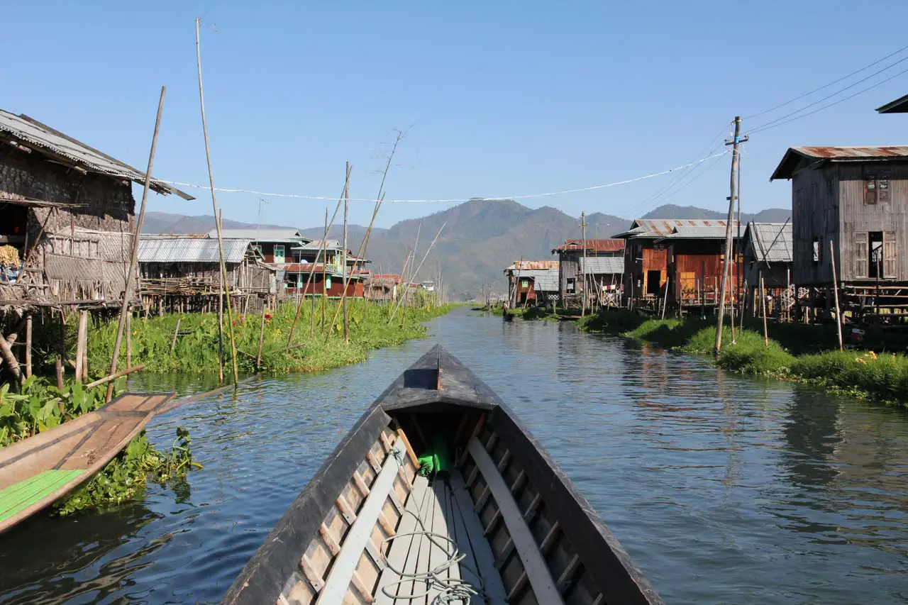 Bow of boat with stilted houses on Lake in foreground and mountains in background