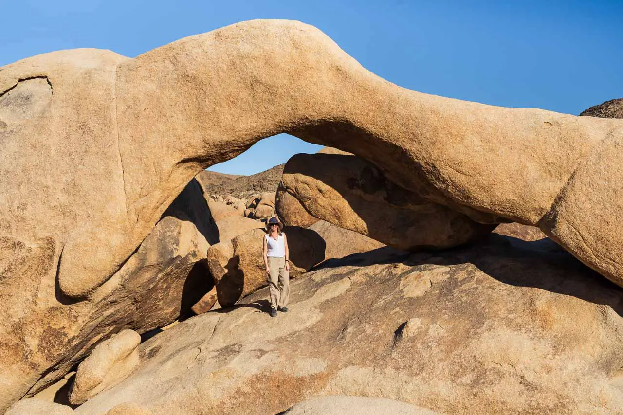 Woman standing under Arch Rock with blue sky and boulders in background