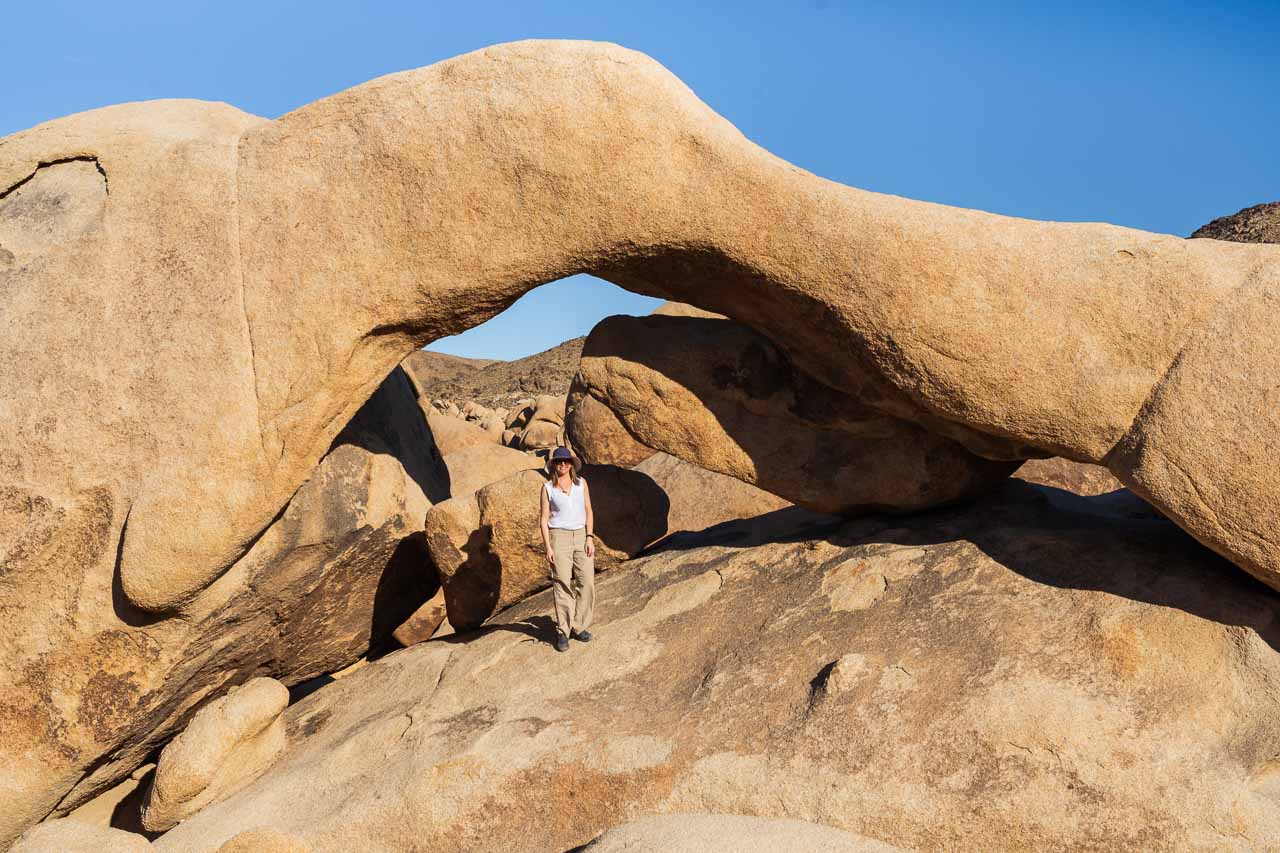 Woman standing under Arch Rock with blue sky and boulders in background